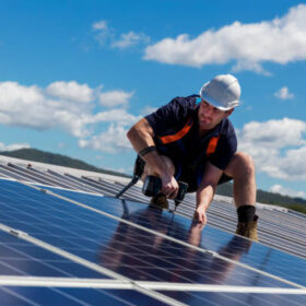 Solar panel installer with drill installing solar panels on roof on a sunny day